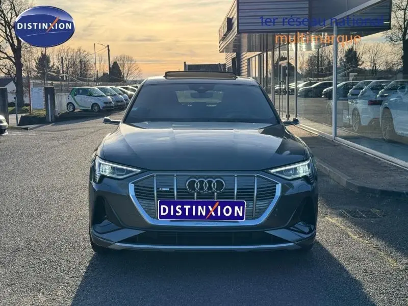 Vue avant d'un Audi E-Tron Sportback 50 S Line gris foncé métal, avec calandre distinctive et phares LED allumés.