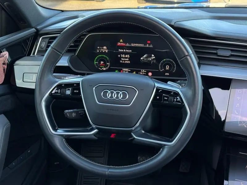 Vue intérieure centrée sur le volant cuir multifonction de l'Audi E-Tron Sportback gris foncé avec tableau de bord numérique.