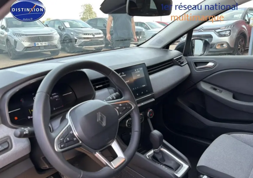 Vue intérieure côté conducteur de la Renault Clio V gris, volant multifonction et tableau de bord moderne avec écran tactile.