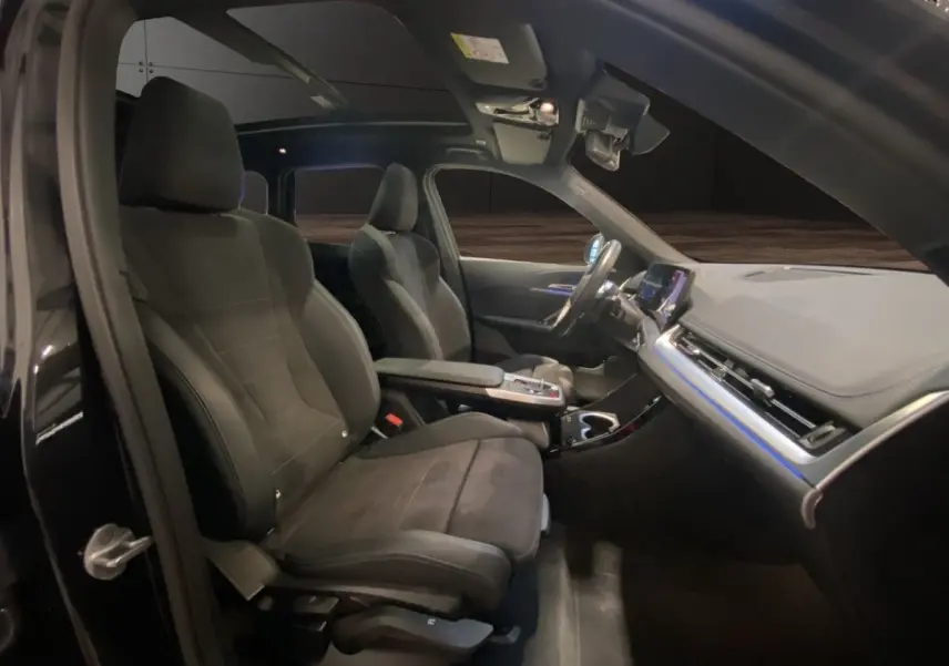 Vue intérieure côté conducteur du BMW X1 noir 2025, mettant en valeur les sièges sport et le tableau de bord moderne avec écran tactile.