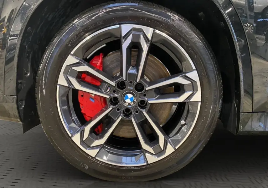 Gros plan sur la roue avant gauche noire d'une BMW X1 2025 avec étrier de frein rouge et jante alu bicolore M Sport.