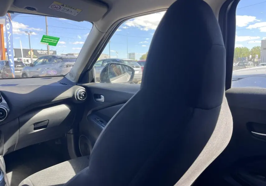 Intérieur de Nissan Juke 2023 vu côté passager, siège tissu noir et tableau de bord gris foncé.