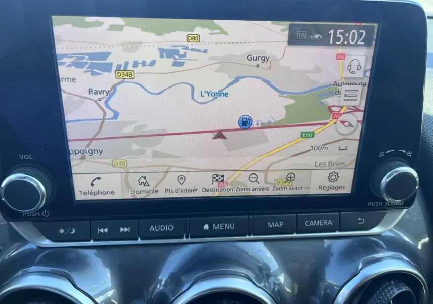 Écran tactile central du Nissan Juke 2023 affichant la navigation GPS avec commandes audio et caméra en dessous.