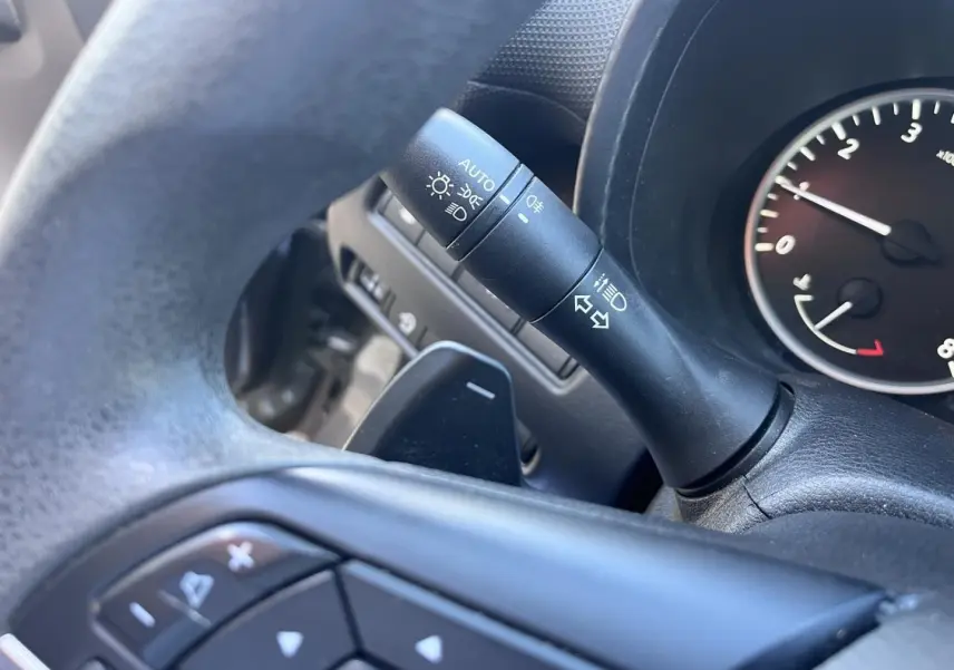 Gros plan sur la commande de clignotants et palettes au volant noir du Nissan Juke gris Argile 2023.