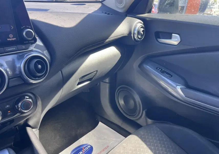 Vue intérieure côté passager du tableau de bord et porte d’une Nissan Juke 2023 avec sellerie tissu noir et finitions argentées.