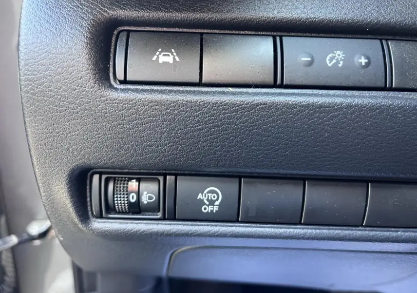 Gros plan sur les commandes de réglage des phares et d'aide à la conduite dans un Nissan Juke gris argile 2023.