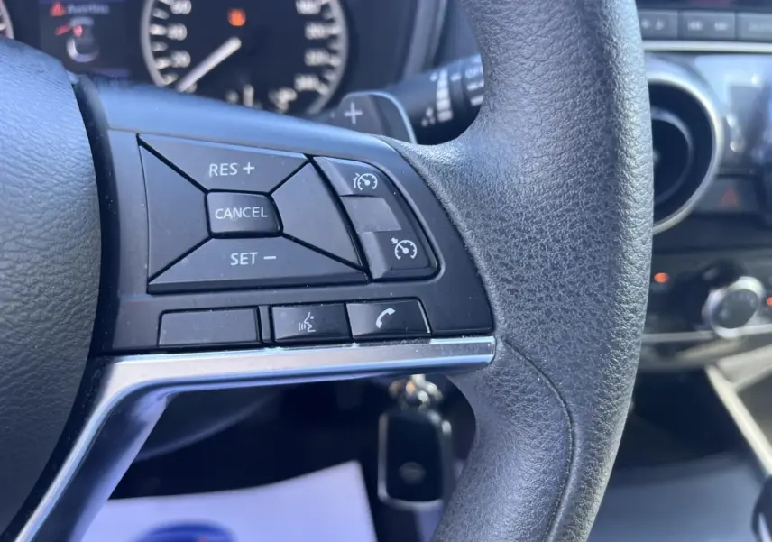 Gros plan sur les commandes au volant noir du Nissan Juke 2023, avec tableau de bord et écran tactile en arrière-plan.