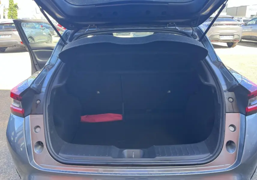 Coffre ouvert vu de l'arrière d'un Nissan Juke 2023 gris Argile Spéciale avec un objet rouge à l'intérieur.