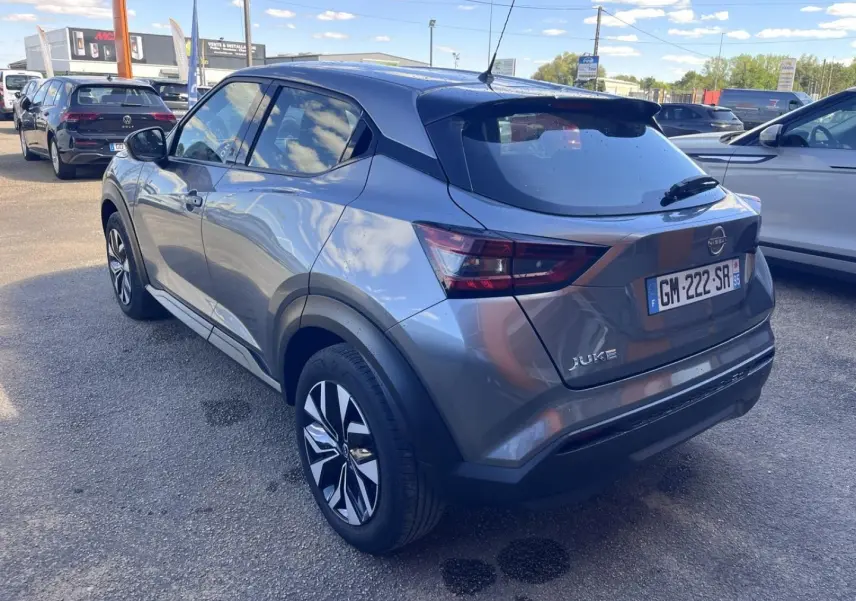 Nissan Juke 2023 gris argile vue 3/4 arrière droit avec jantes bi-ton et toit noir brillant.