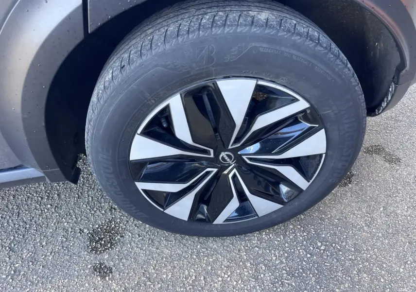 Gros plan sur la roue avant droite d’une Nissan Juke 2023 gris argile avec jante alliage bicolore.