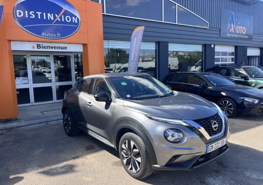 Nissan Juke gris Argile Spéciale vue 3/4 avant droit, avec calandre V-Motion et jantes bi-ton visibles.