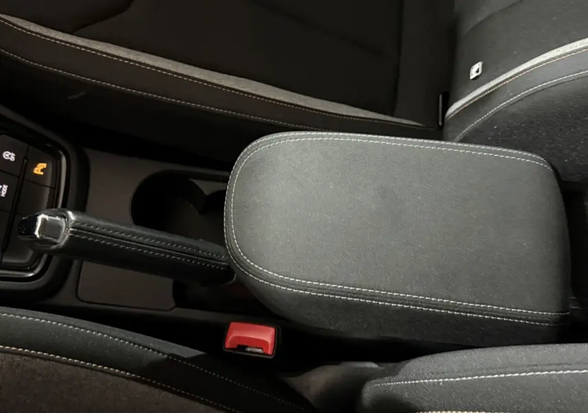 Vue plongeante sur l'accoudoir central noir et frein à main cuir du Skoda Kamiq 2024, version essence rouge.