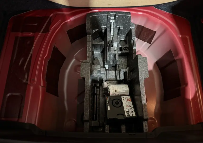 Vue plongeante sur le coffre rouge du Skoda Kamiq 2024, montrant le rangement sous plancher avec kit de réparation pneus.