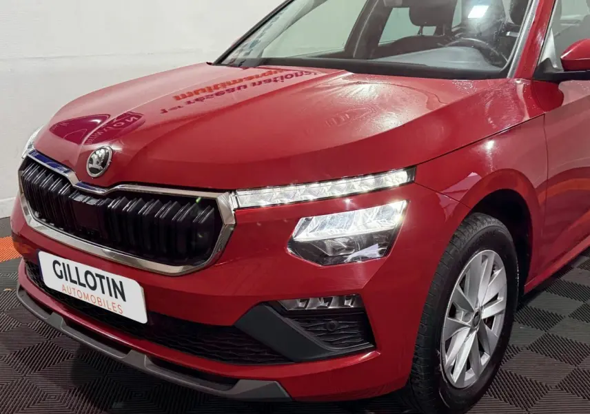 Vue 3/4 avant droit d’un Skoda Kamiq rouge avec calandre noire et phares LED allumés.