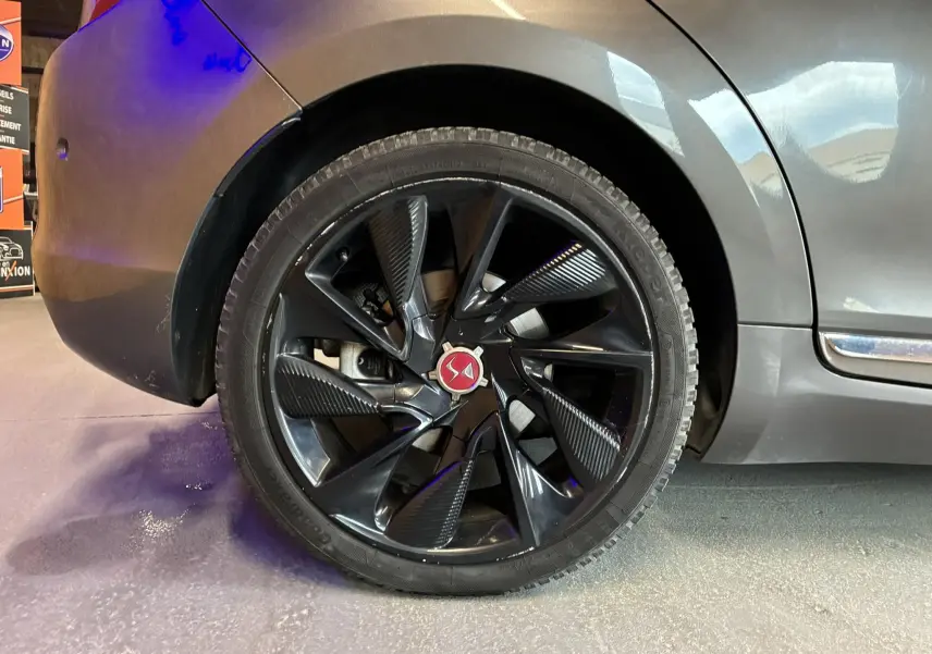 Gros plan sur la roue arrière gauche d'une DS5 gris métallisé, mettant en valeur la jante noire au design moderne.