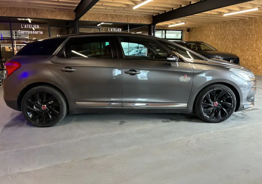 Vue de profil droit d'une DS5 gris métallisé avec jantes noires et détails chromés, stationnée en intérieur.