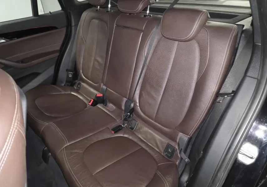 Vue intérieure sur la banquette arrière en cuir marron perforé du BMW X1 xDrive 25d noir, avec ceintures de sécurité visibles.