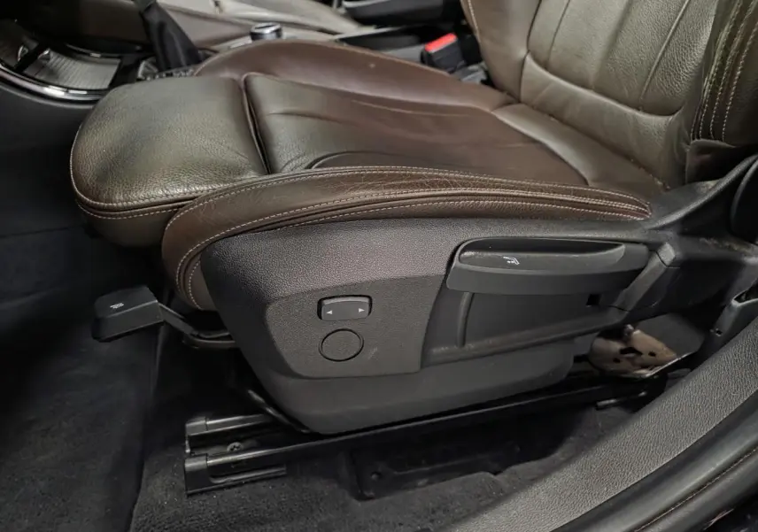 Gros plan sur le siège avant conducteur en cuir marron perforé avec commandes d'ajustement électrique sur BMW X1 noir.