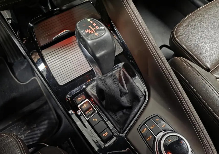 Gros plan sur la console centrale noire brillante avec levier de vitesses et commandes du BMW X1 xDrive 25d 2016 en cuir marron.