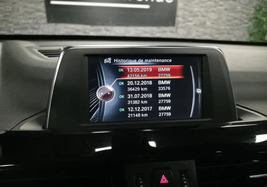 Écran central de la BMW X1 xDrive 25d 2016 affichant l'historique de maintenance dans l'habitacle noir.