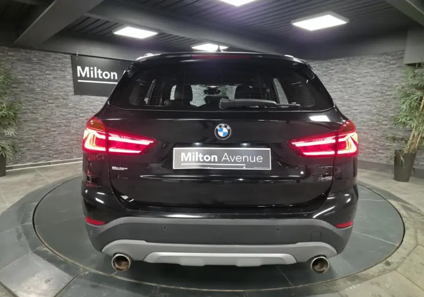 Vue arrière d'un BMW X1 xDrive 25d noir avec feux allumés et double sortie d'échappement chromée.