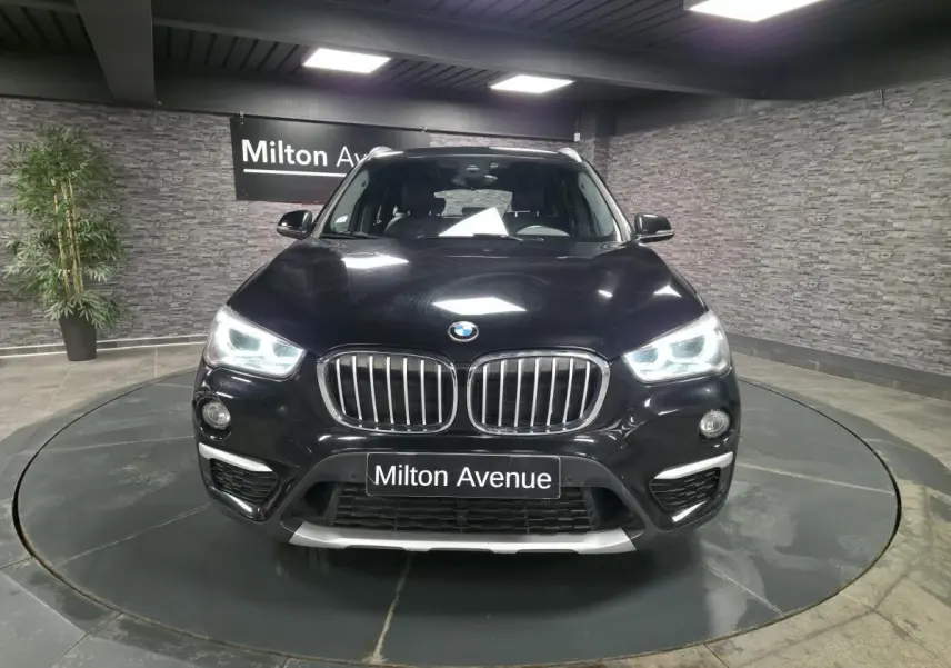 BMW X1 xDrive 25d noir vue de face avec calandre chromée et phares LED allumés en showroom.