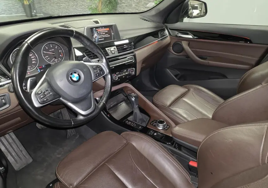 Vue intérieure côté conducteur du BMW X1 xDrive 25d 2016 avec sellerie cuir marron et tableau de bord noir brillant.