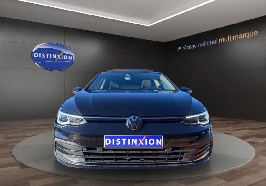 Volkswagen Golf noire vue de face avec toit panoramique et phares LED allumés en showroom.