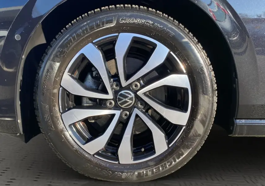 Gros plan sur la roue avant droite d’une Volkswagen Golf noire, jante alliage bicolore avec logo VW central.