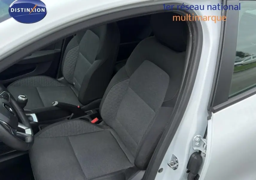 Vue intérieure côté conducteur de la Renault Clio blanc 2021, montrant les sièges en tissu gris et la boîte manuelle.