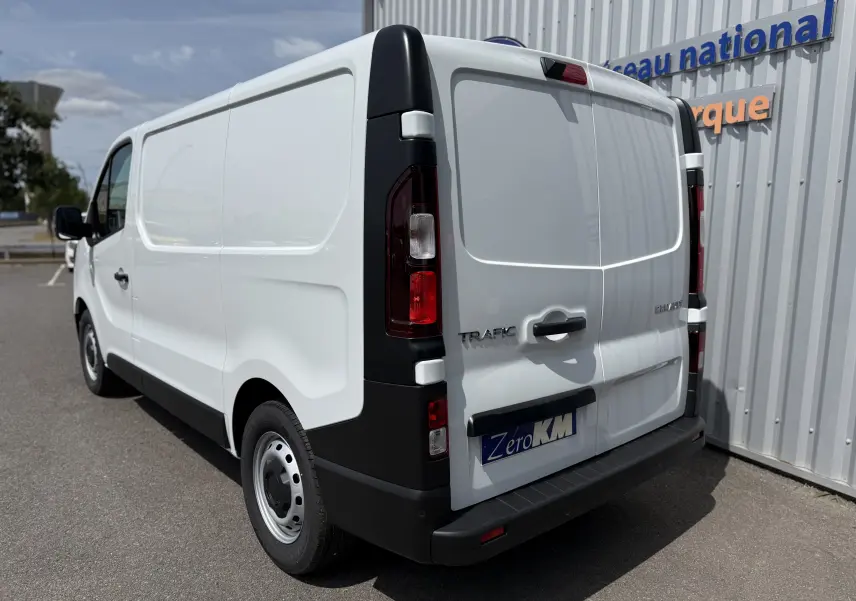 Vue 3/4 arrière droite d’un Renault Trafic Fourgon blanc, avec portes arrière fermées et feux arrière visibles.