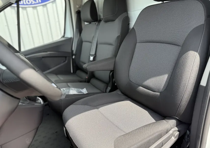 Vue intérieure côté conducteur du Renault Trafic Fourgon blanc 2025, sièges tissu gris avec accoudoir.