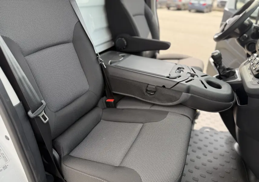 Vue intérieure côté gauche du Renault Trafic Fourgon blanc 2025, montrant les sièges en tissu gris et la console centrale rabattable.