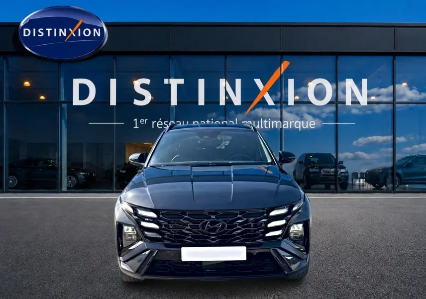 Vue de face du Hyundai Tucson gris ecotronique avec calandre glossy black et feux LED distinctifs devant un showroom Distinxion.