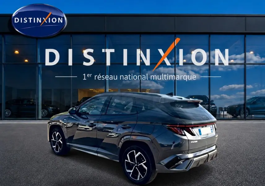 Vue 3/4 arrière droite du Hyundai Tucson 2026 gris ecotronique avec jantes alliage et feux arrière LED, devant une vitrine Distinxion.
