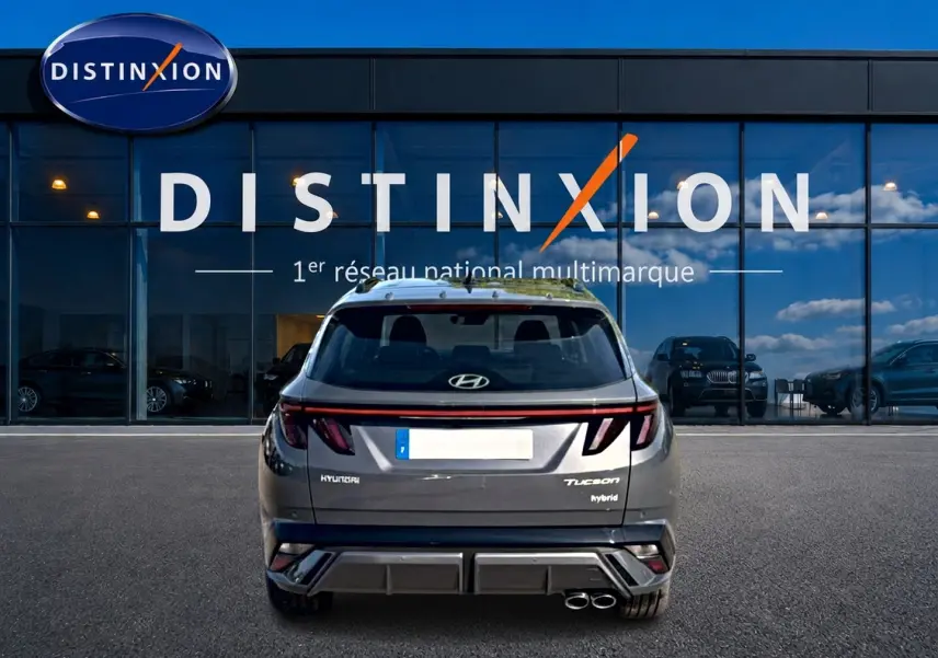 Vue arrière du Hyundai Tucson hybride gris ecotronique avec feux LED et double sortie d'échappement, devant une vitrine Distinxion.
