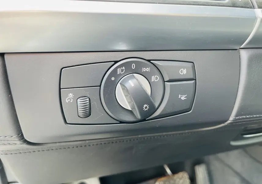Gros plan sur le bouton de commande des phares dans l'habitacle noir du BMW X6 blanc 2013.
