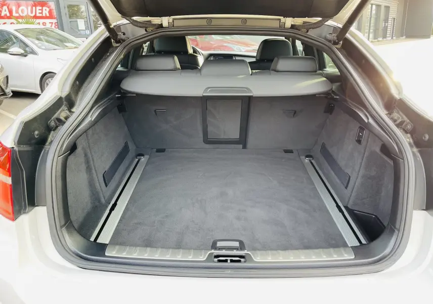 Coffre ouvert en vue arrière d'un BMW X6 blanc, montrant un espace de chargement spacieux et doublure grise.