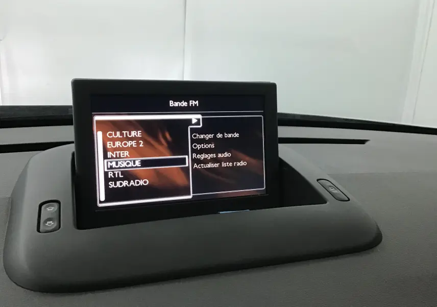 Écran central du tableau de bord du Peugeot 3008 blanc de 2015 affichant le menu radio FM avec plusieurs stations listées.