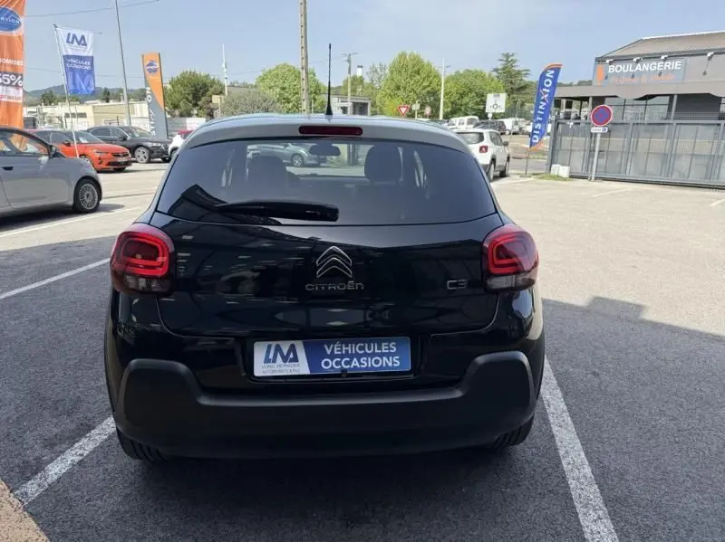 Vue arrière d'une Citroën C3 noire avec toit blanc, en stationnement devant un commerce, plaque "Véhicules Occasions".