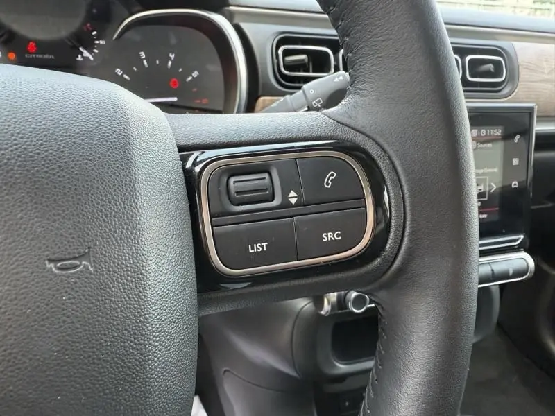 Gros plan sur les commandes du volant côté gauche d'une Citroën C3 noire avec toit blanc, tableau de bord et écran tactile visibles.