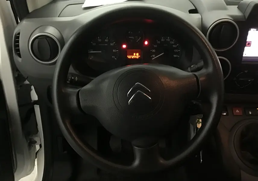 Vue intérieure centrée sur le volant noir d'un Citroën Berlingo blanc 2018 avec tableau de bord et compteur allumé.