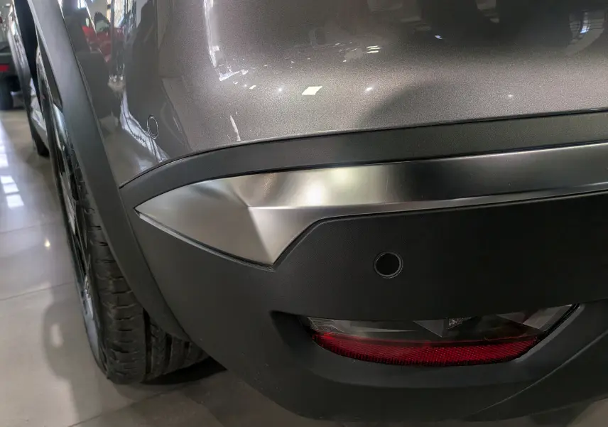 Gros plan sur le pare-chocs arrière droit gris Cassiopé du Renault SYMBIOZ E-Tech, avec feu et capteur de recul visibles.