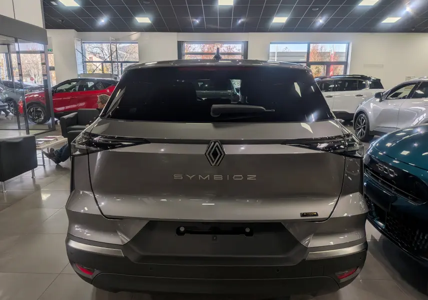 Vue arrière du Renault SYMBIOZ gris Cassiopé en hybride, avec logo et feux arrière étirés en intérieur showroom.