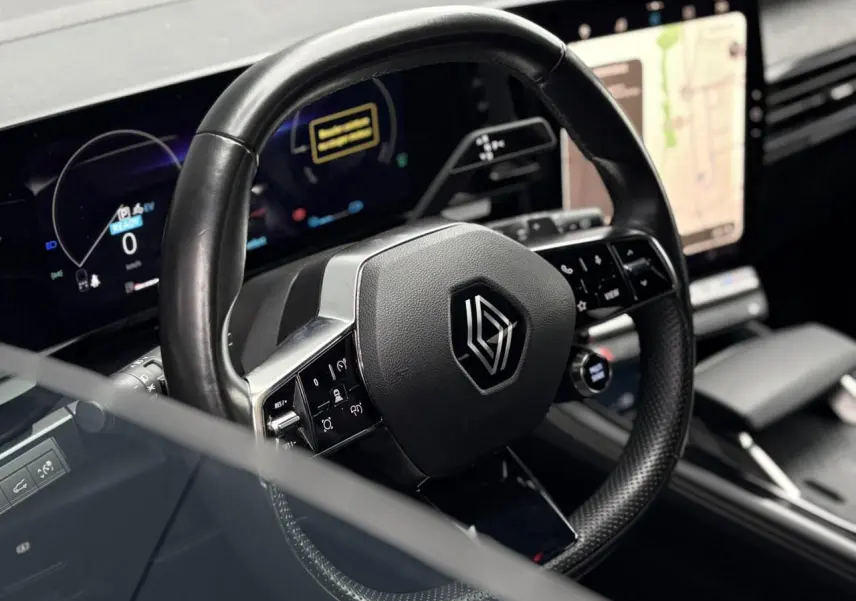 Vue rapprochée du volant noir de la Renault Espace 2024 avec commandes intégrées et écran tactile en arrière-plan.