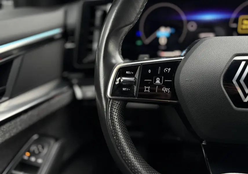Gros plan sur le volant noir perforé avec commandes intégrées du Renault Espace 2024, intérieur sombre.
