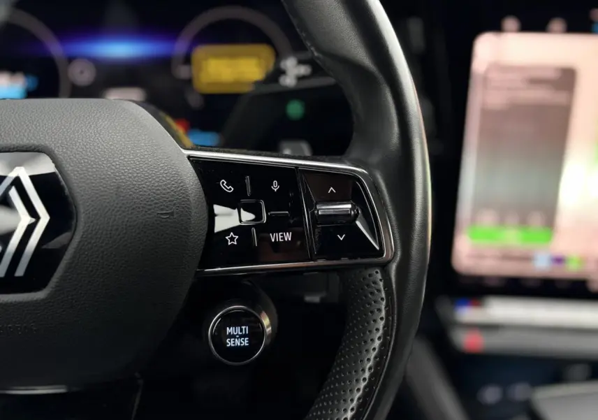 Gros plan sur le volant noir perforé du Renault Espace 2024 avec commandes multifonctions et bouton Multi-Sense éclairé.