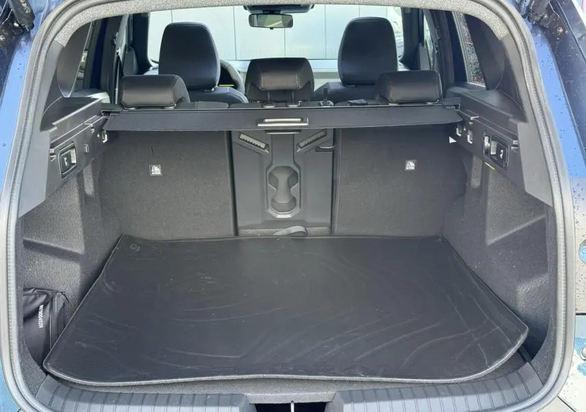 Coffre ouvert vu de l'arrière du Dacia Bigster bleu indigo, avec tapis de protection et banquette arrière visible.