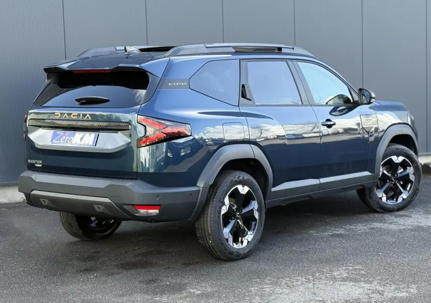 Vue 3/4 arrière droite du Dacia Bigster bleu indigo avec jantes alliage noires et hayon électrique visible.