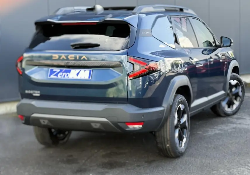Vue 3/4 arrière droite d'un Dacia Bigster bleu indigo avec jantes alliage noires et hayon électrique visible.